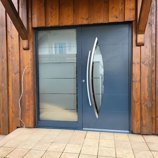 Aluminium-Haustür in RAL 7016 Anthrazitgrau mit augenförmigem Glasausschnitt und geschwungenen Edelstahl-Applikationen